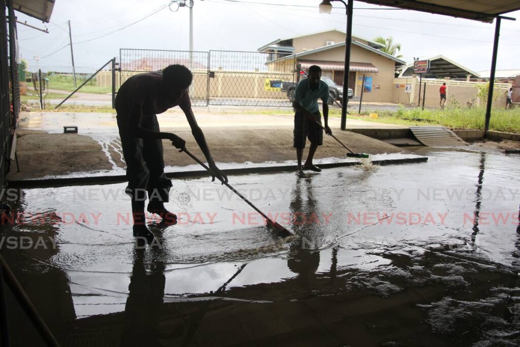 Two men sweep out water from the Baig residence on Pluck Road, Woodland, on Thursday. - Lincoln Holder