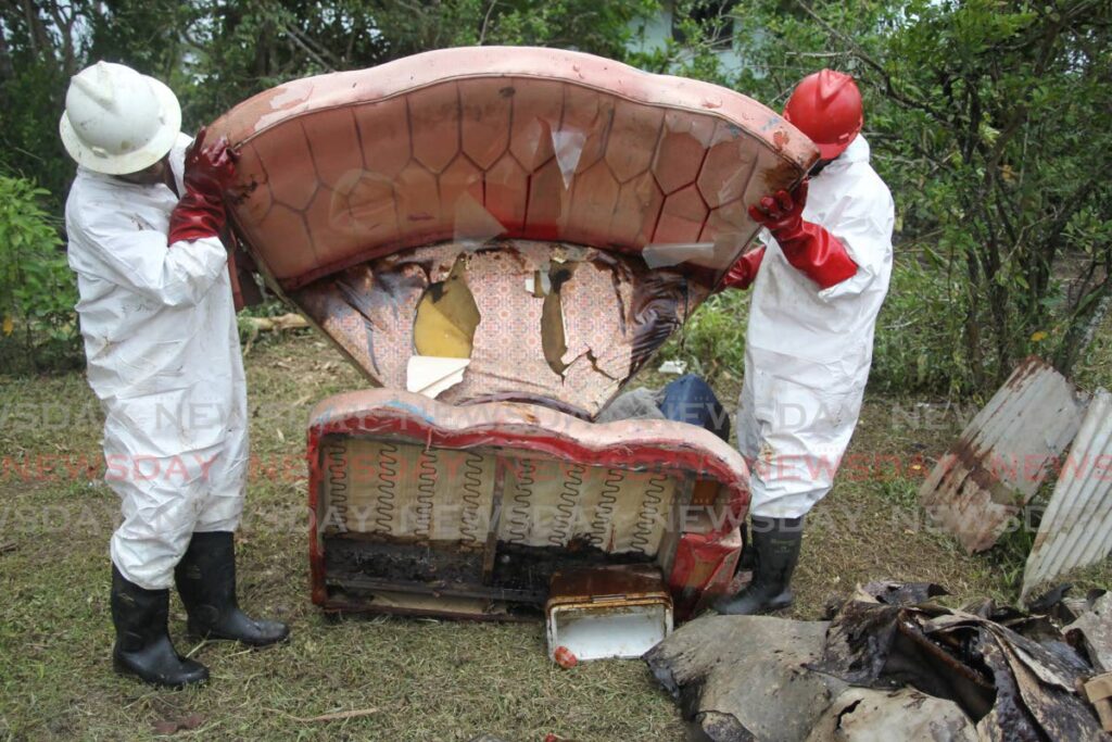 Adrian Thomas and Zakeer Mohammed, employees of ARAV Construction Services contracted by Heritage to clean up the oil spill at Katwaroo trace and Ramdharry Trace in Penal ,remove oil soaked furniture from the home of Usha Boodram on Friday. - Lincoln Holder