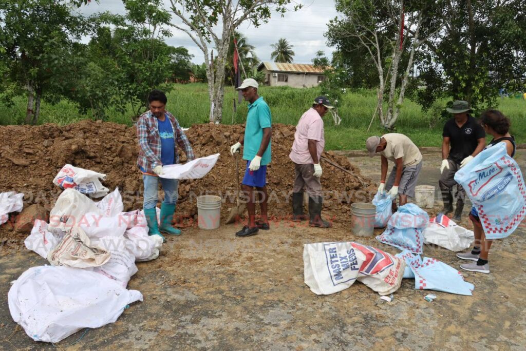 Woodland residents fill sandbags to be used in an effort to reinforce the banks of the New Cut River in Penal on Sunday. PHOTO BY ROGER JACOB - 