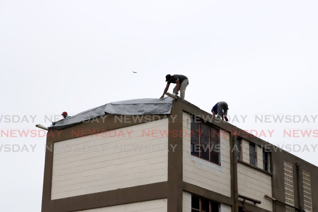 Workmen secure tarpaulin to the top of the HDC housing complex in Trou Macaque, Laventille on Tuesday after the roof was ripped off by strong winds.  - 
