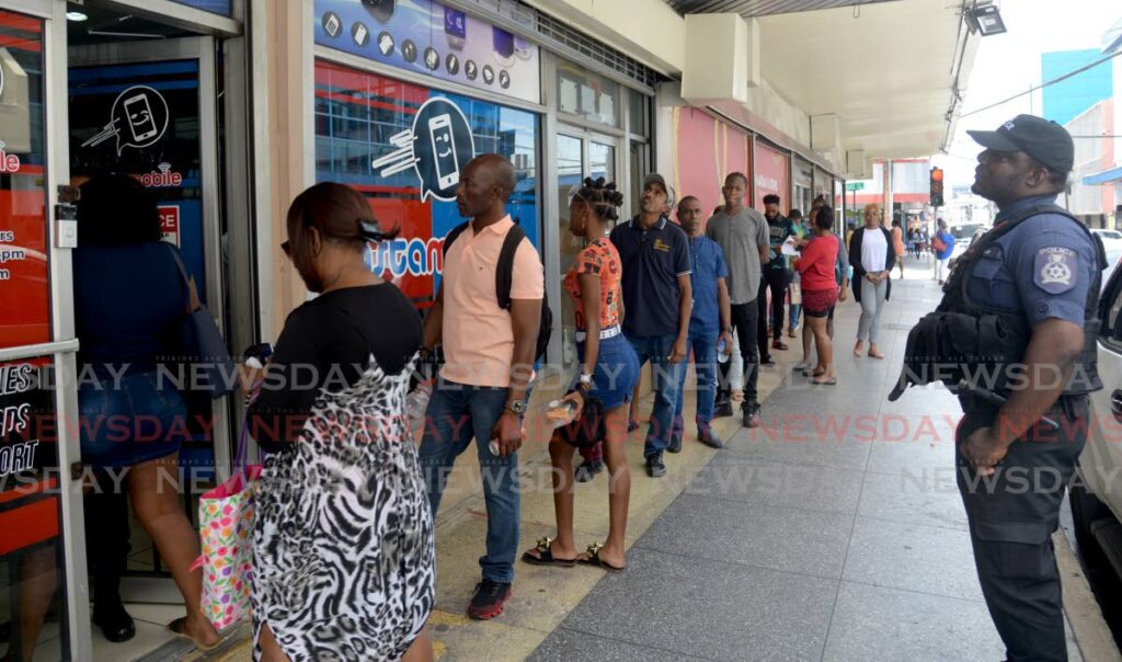 A policeman keeps watch as customers wait to enter InstaMobile store for a sale on cell phones on Frederick Street, Port of Spain on Friday. - Anisto Alves