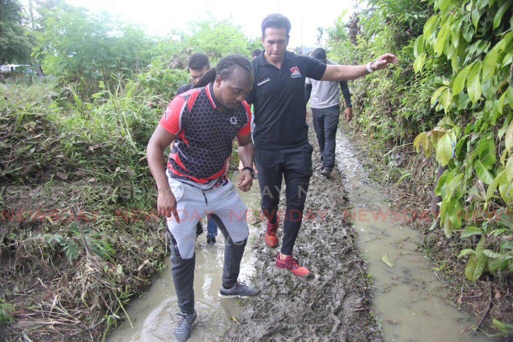 Rural Development and Local Government Minister Faris Al-Rawi tries to keep his balance while walking along a muddy path in Green Acres, San Fernando where he met with residents affected by flooding on Saturday.Photo by Lincoln Holder