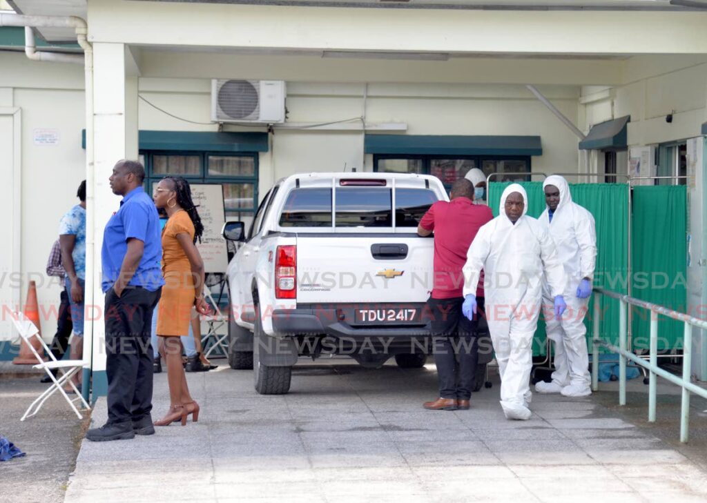 Undertakers, in white suits on the right, at the Cunupia Health Centre where security officer Hasley Augustine died after he was shot during a robbery at DS Plaza on Thursday. - Anisto Alves