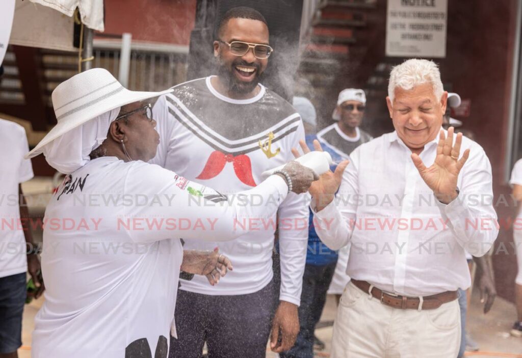 Pan Trinbago president Beverley Ramsey-Moore throws powder on outgoing Port of Spain mayor Joel Martinez as incoming Port of Spain mayor Chinua Alleyne looks on at the Pan and Powder parade port of Spain on August 23 - Photo by Jeff K. Mayers