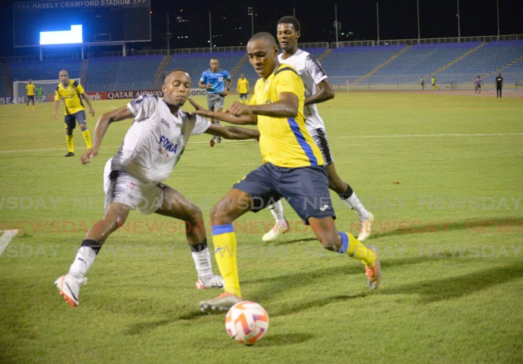 Defence Force FC, midfielder, Reon Moore, yellow, pushes the ball past Cavalier FC, defender, Adrian Reid, during their Concacaf Caribbean Cup march at the Hasley Crawford Sadium, Port of Spain on August 24 - Anisto Alves