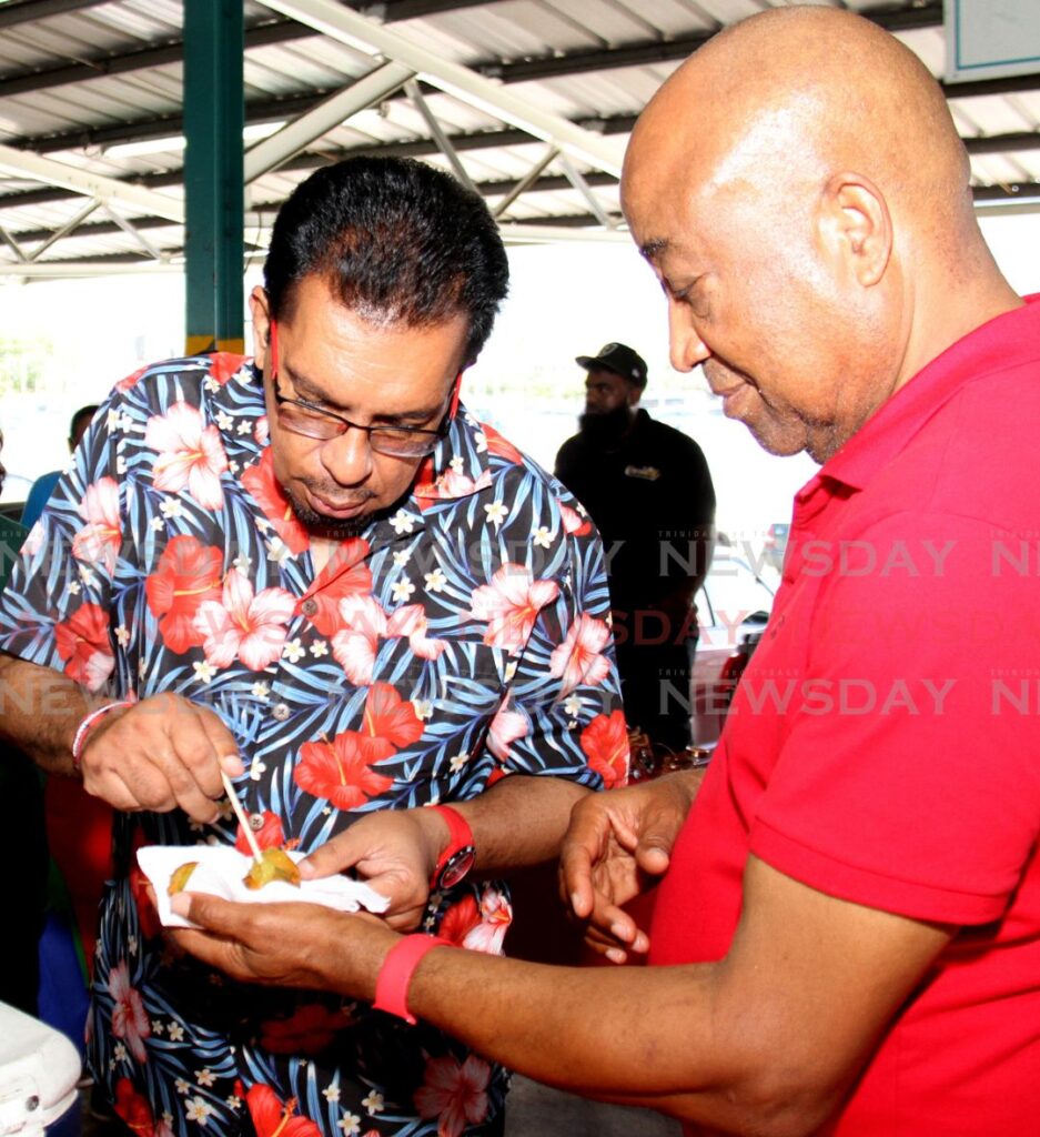 Agriculture Minister Kazim Hosein, left, and chairman of NAMDEVCO Wayne Innis try mango pholourie made by Sabrina Nicholls of Sabrina's Exotic Caribben Fusion of at the Norris Deonarine Northern Wholesale Market, Macoya. - Photo by Ayanna Kinsale