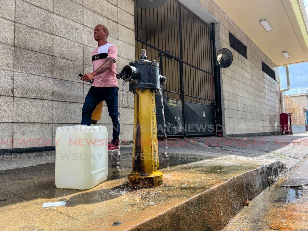 In this April file photo, a pedestrian walks past a leaking fire hydrant along Park Street, Port of Spain.  - Jeff Mayers