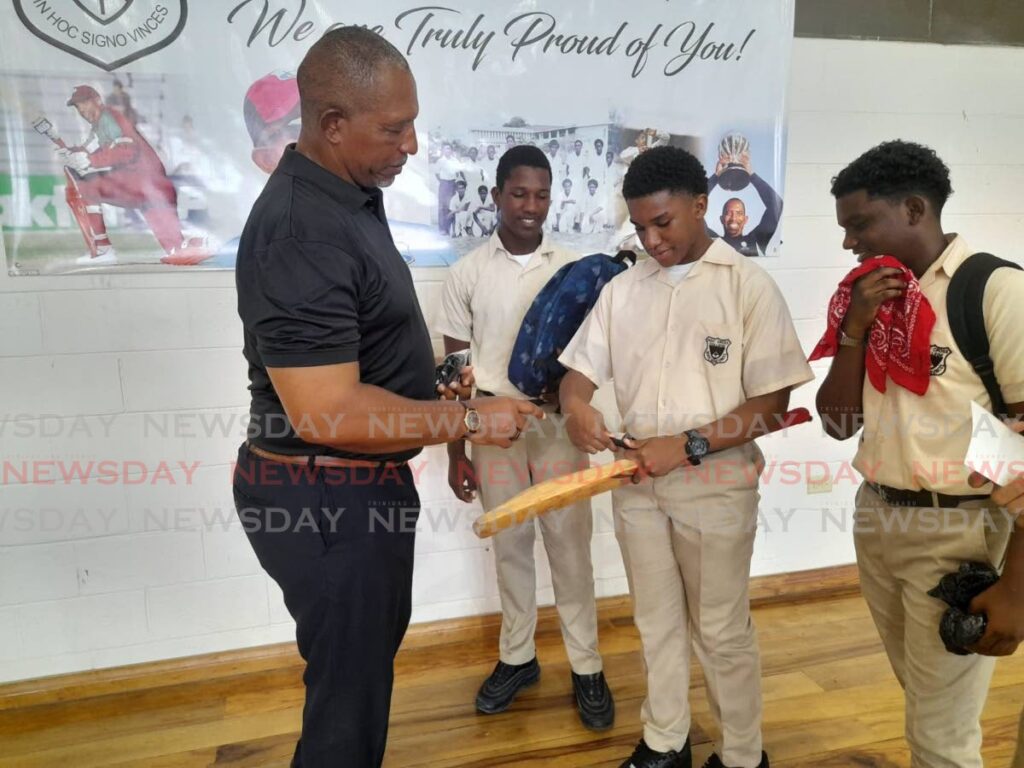 Former West Indies player and head coach Phil Simmons(L) autographs a a bat for a student of his alma mater Holy Cross College, at the college auditorim, in Arima, on Thursday.  - Photo by Roneil Walcott 
