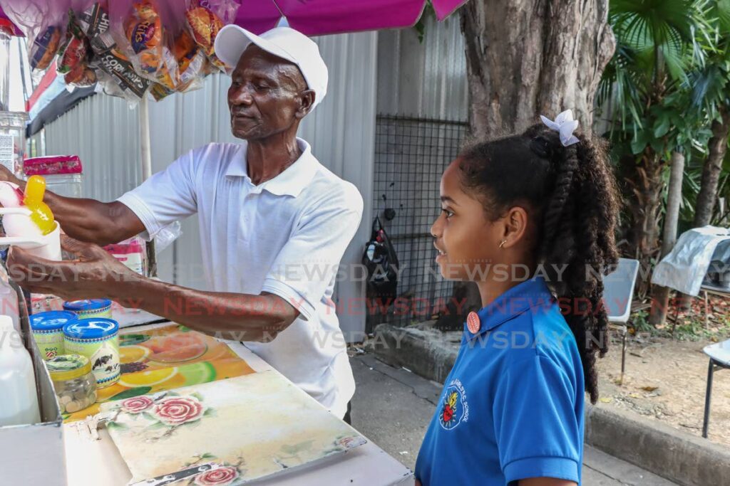 Mr Jack of J&K Snow Cones prepares one for nine-year-old Sacred heart Girls’ RC School student Adell Quash on Upper Frederick Street, Port of Spain, on Friday. - Photo by Jeff Mayers