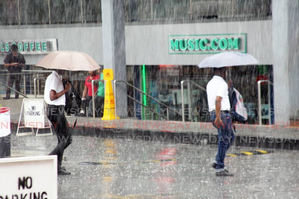 Pedestrians take shelter under umbrellas during a sudden shower in San Fernando on Wednesday. A hot spell alert has since been discontinued by the TT Meterological Service. - Lincoln Holder