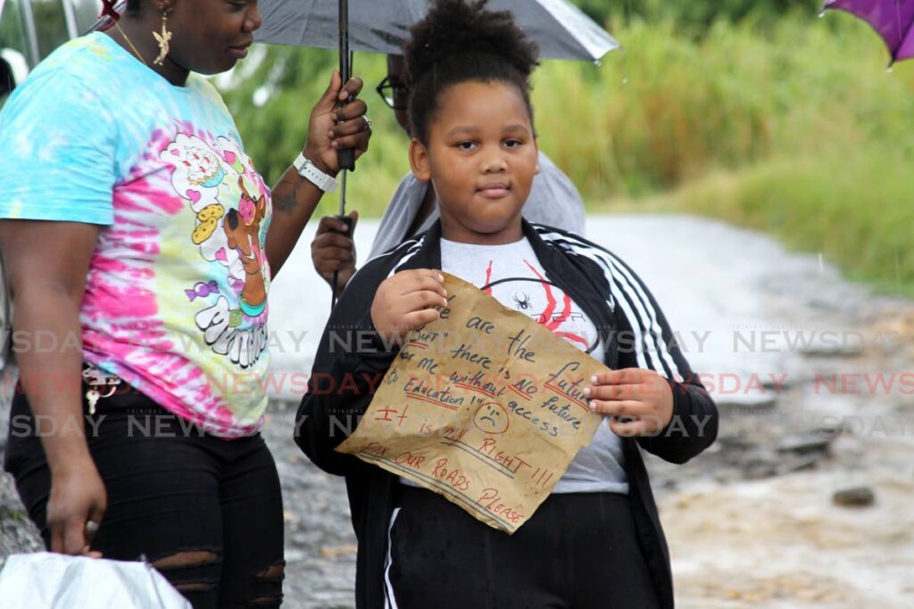 A Student from the Caratal Sacred Heart RC hold a placard highlighting concerns over the road conditions near the school. - Photo by Lincoln Holder