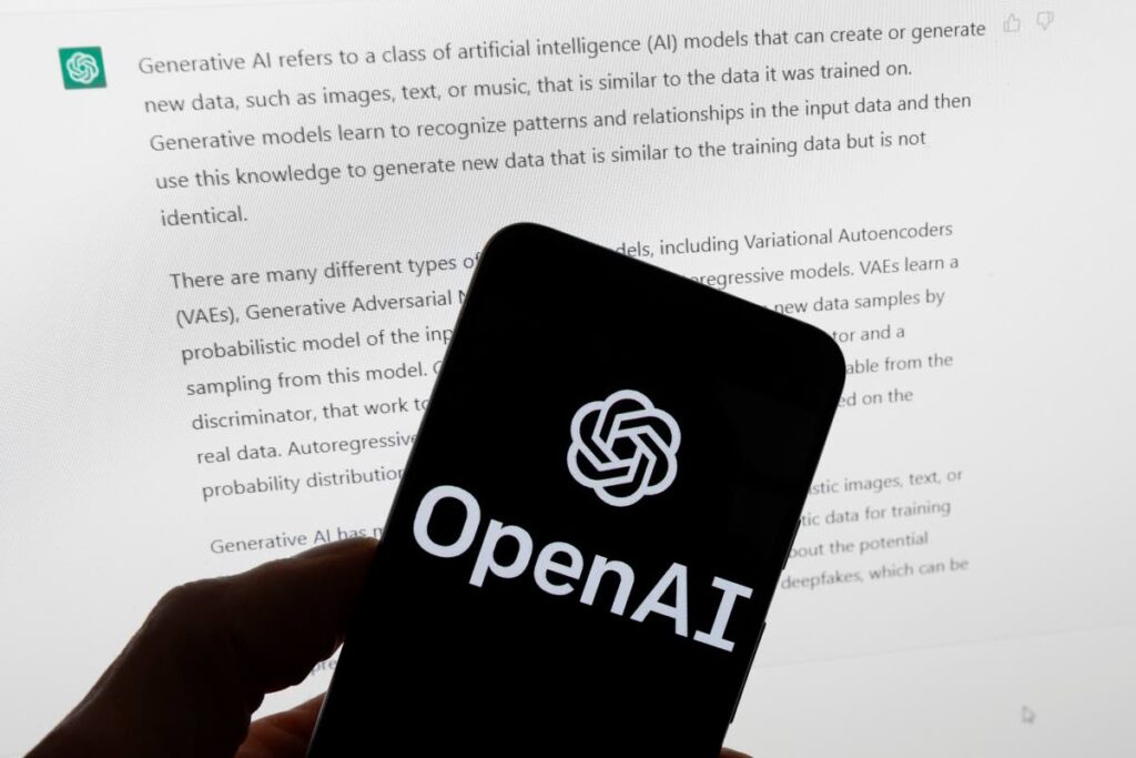 The OpenAI logo is seen on a mobile phone in front of a computer screen displaying output from ChatGPT. AP PHOTO - 