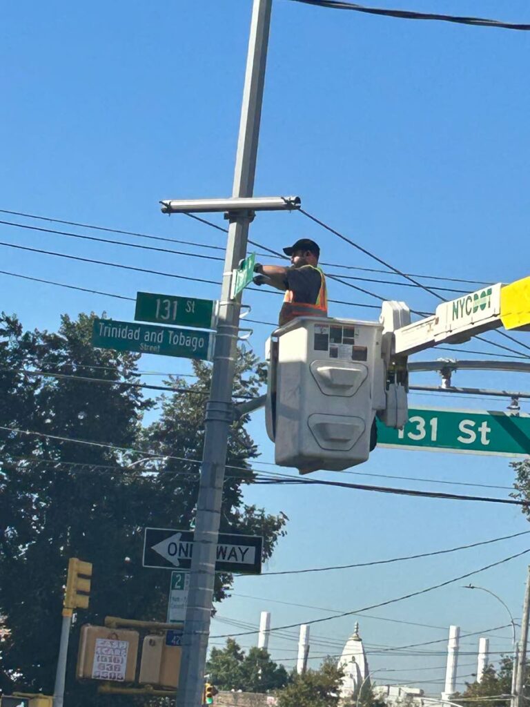A worker installs a new Trinidad and Tobago Street sign at Queens, New York.  - 