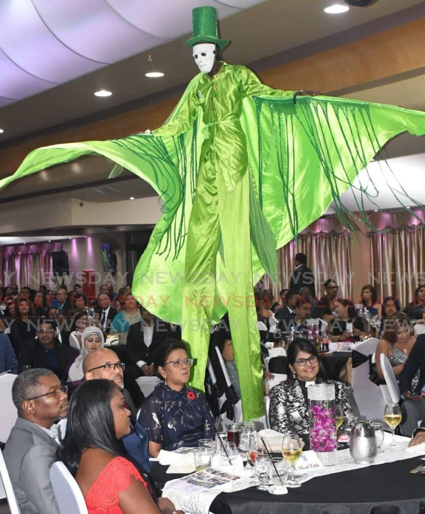 A JUMBIE PROWLS: President Christine Kangaloo sat apparently unaware that a green Moko jumbie was prowling right behind her at the Achievors Banquet Hall in San Fernando during the Rapidfire Kidz Foundation's gala event on Saturday evening.  - Photo by Yvonne Webb