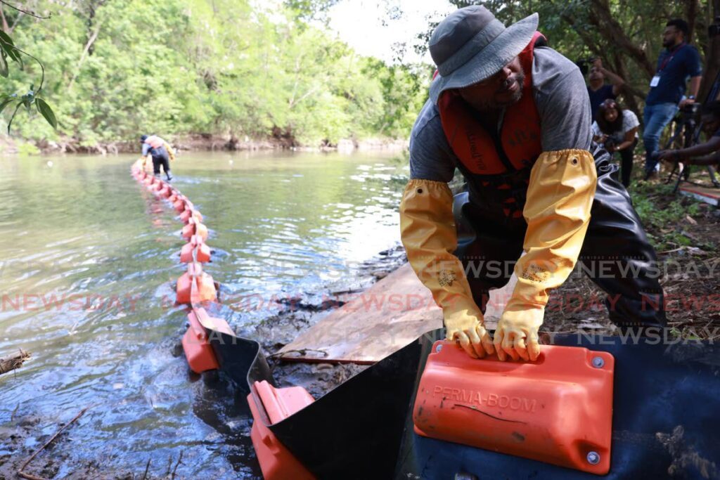 A member of the Rotary Club of Port of Spain West places a boom in the Maraval River on Wednesday.  - Jeff K. Mayers