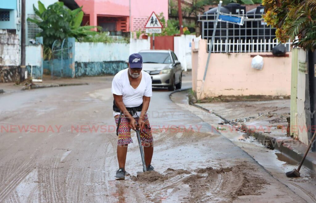 St Francois Valley Road, Belmont, resident Ancil Luke shovels mud from the road in front of his home after flash floods on Sunday. - Angelo Marcelle