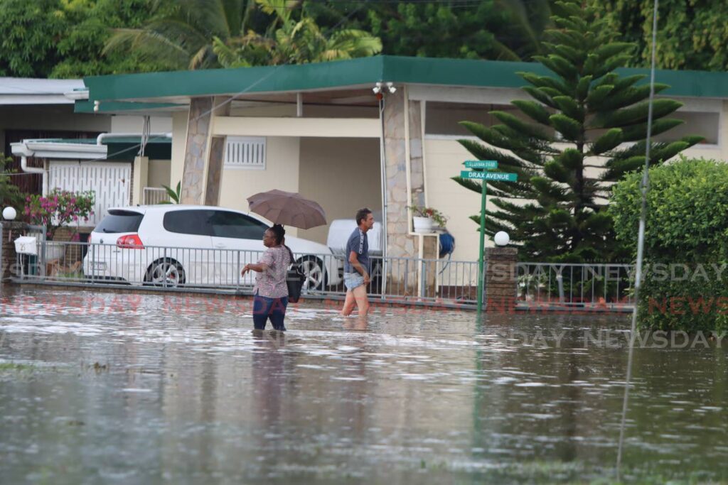 A woman and a man walk through a flooded area of Savannah Drive, Trinicity, on Wednesday. - Angelo Marcelle