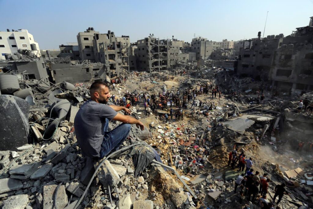 A man sits on the rubble as others wander among debris of buildings that were targeted by Israeli airstrikes in Jabaliya refugee camp, northern Gaza Strip. AP PHOTO - 