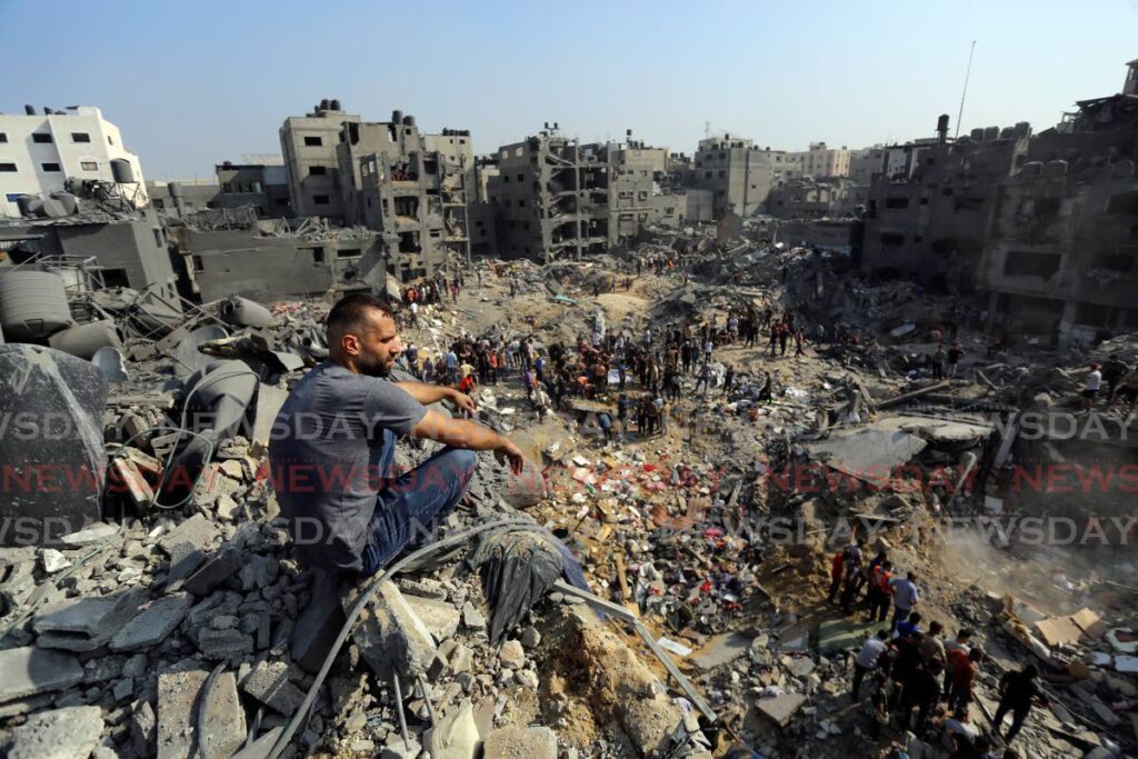 A man sits on the rubble as others wander among debris of buildings that were targeted by Israeli airstrikes in Jabaliya refugee camp, northern Gaza Strip. AP PHOTO - 
