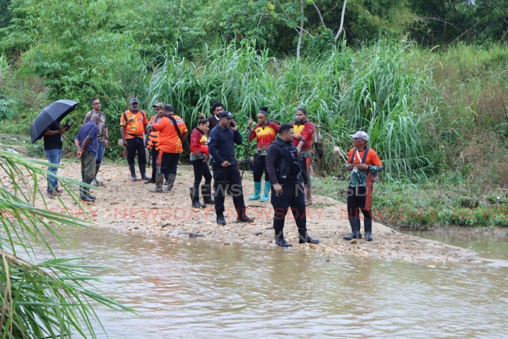 Members of the Hunter’s Search and Rescue Team, Sham’s Commanders and the police stand on the Mausica river bank near Printryville on Tuesday, where the body of a man that washed down the drain and into the river on Monday was found. - Angelo Marcelle