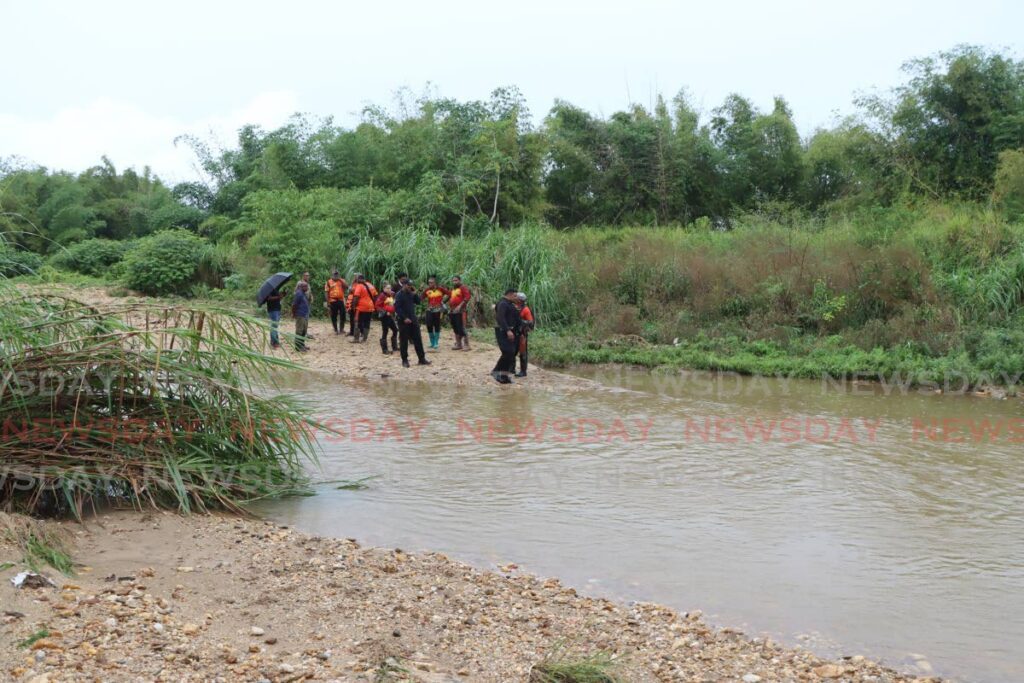 Members of the Hunter's Search & Rescue Team, Sham's Commanders and the Trinidad & Tobago Police Service, stand on the Mausica river bank in the vicinty of Printryville, where the body of a man that washed down the drain on M onday and into the river was found on Tuesday - Photo by Angelo Marcelle