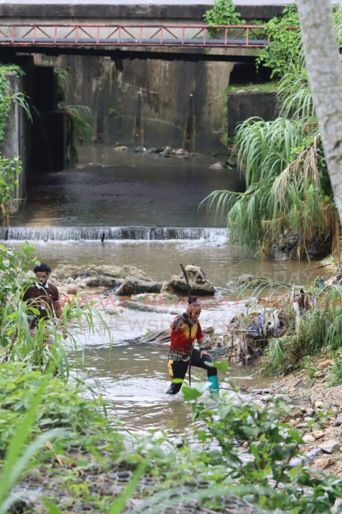 Members of Sham's Commanders cross the Mausica River on Tuesday in search of a man that washed down the drain and into the river on Monday. The man's still unidentified body was found later Tuesday. - Angelo Marcelle