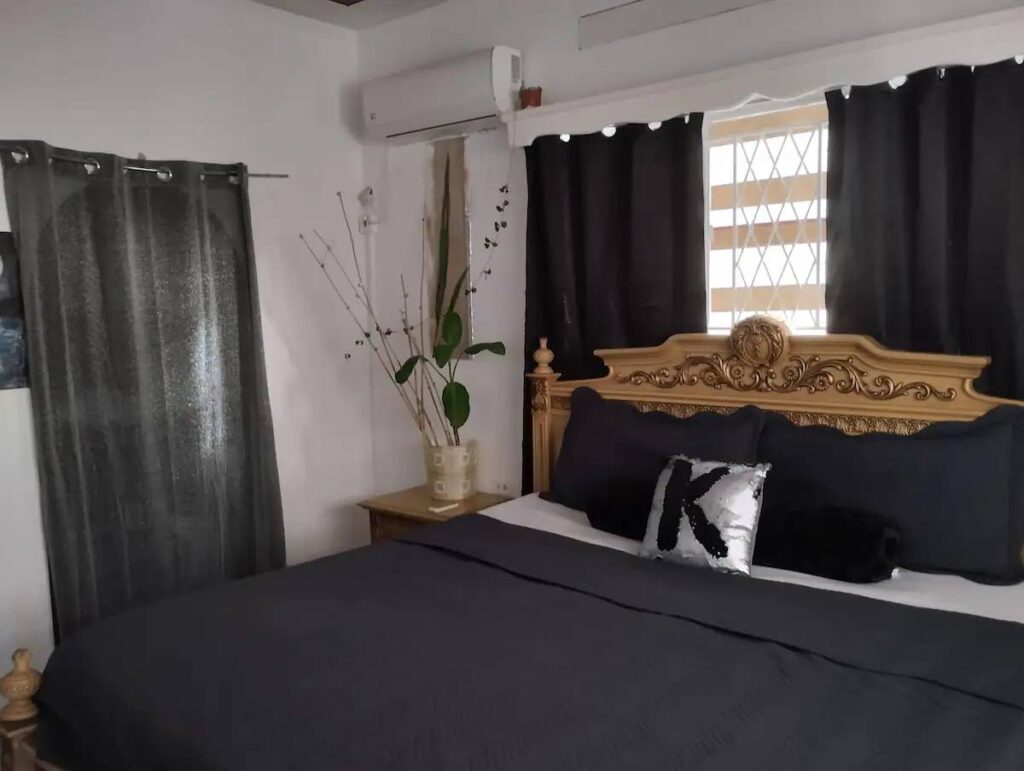 City Rental: A dark themed bedroom with a king-sized bed. The sequenced pillow is a personal touch for the incoming guest whose name begins with the letter K. - 