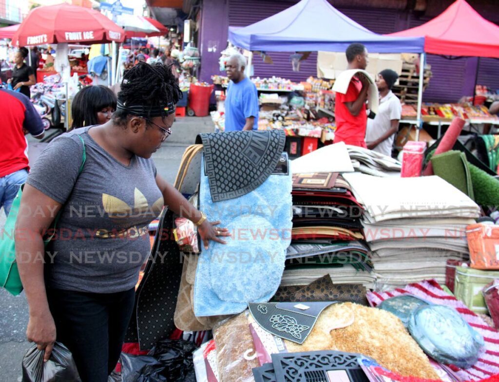 A shopper inspects mats on sale on Charlotte Street, Port of Spain on Tuesday. - AYANNA KINSALE