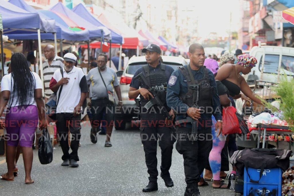 Police officers patrol as shoppers go about their business in downtown Port of Spain.  Photo by Roger Jacob