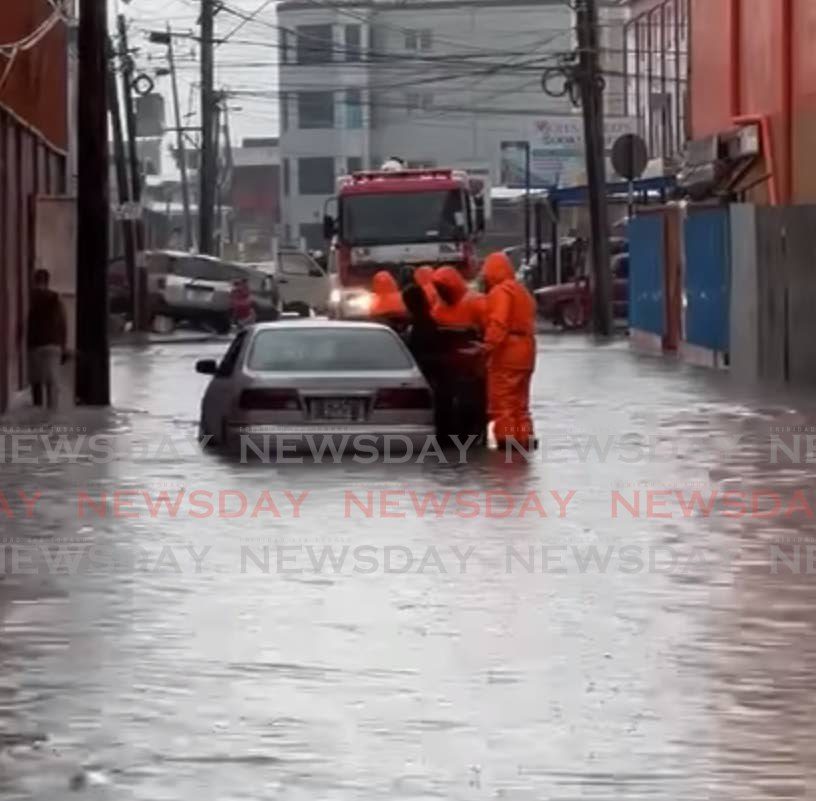 A screenshot from a video posted on social media showing fire officers rescuing a woman and her children from their car after it stalled in flood waters in Chaguanas on Thursday.  -  