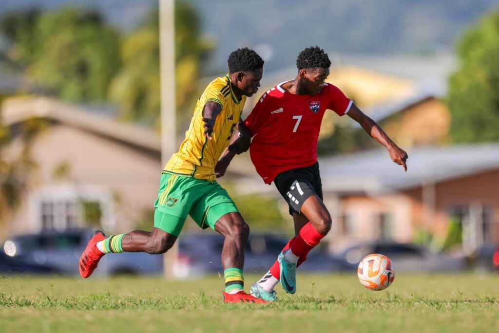 TT’s Jlon Matthews (R) goes around Jamaica’s Rolando Barrett during Under-20 practice match at the UTT O’meara on Thursday, in Arima.  -Photo by Daniel Prentice 