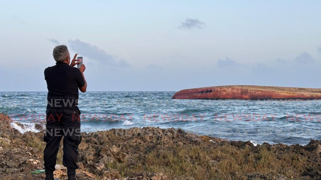A man takes a picture of a mystery boat which was found overturned near Cove on February 7. The National Security Ministry says another vessel, a tug boat, was involved in the incident.  - FILE PHOTO 
