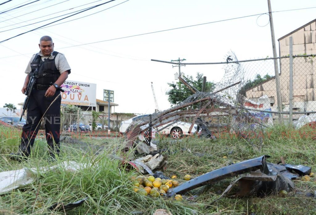This police officer looks at a heap of oranges left at the scene where a vehicle lost control, killing Prematee Laltoo and injuring Hakeem Bain and his mother Alana Bain at Southern Main Road on February 22. - Photo by Ayanna Kinsale