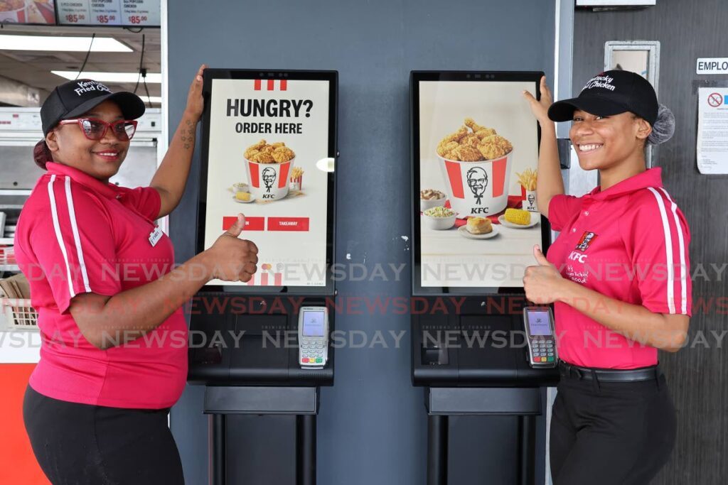 KFC employees Faria Khan and Kayla Wright, pose infront of the newly installed digital kiosks at the South Park, San Fernando branch. - Photo by Lincoln Holder