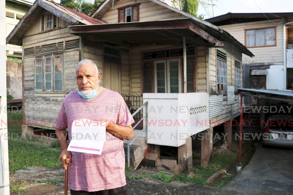 Steve Khan of Panco Lane, San Fernando, stands in front of his wooden home holding his property tax document. - File photo by Lincoln Holder