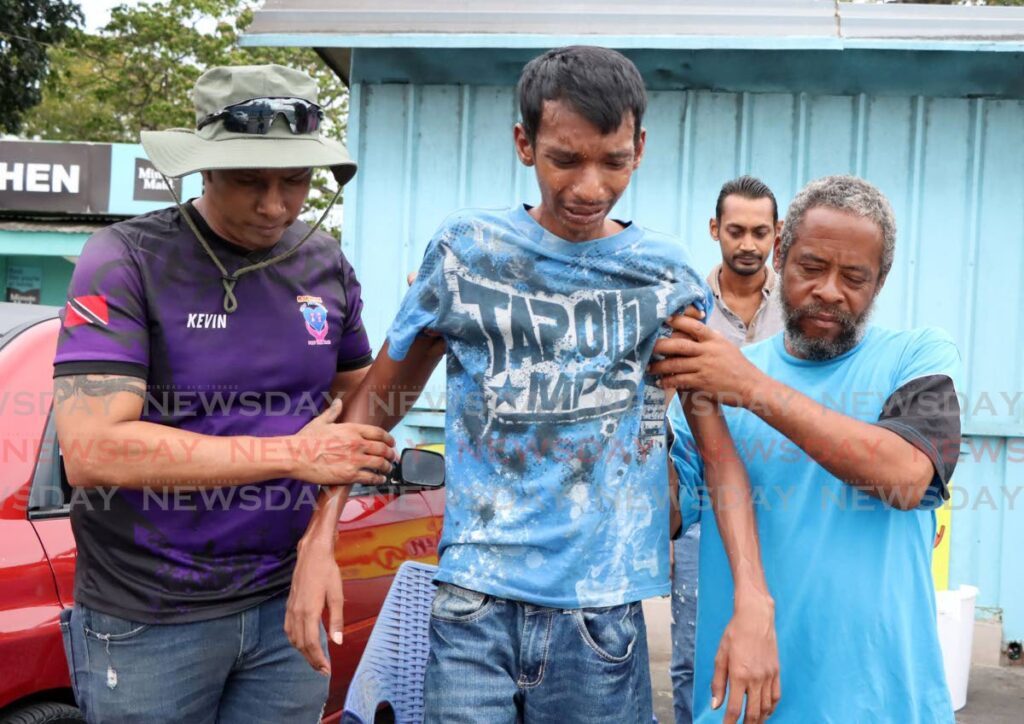 Salesman Jeffrey Ramroop is assisted by Rapidfire Kidz Foundation president Kevin Ratiram, left, and an unidentifed man after he was attacked by a swarm of bees while selling his kites at Palmiste Park, San Fernando on Monday. Ramroop and three other were hospitalised after the incident.  - AYANNA KINSALE