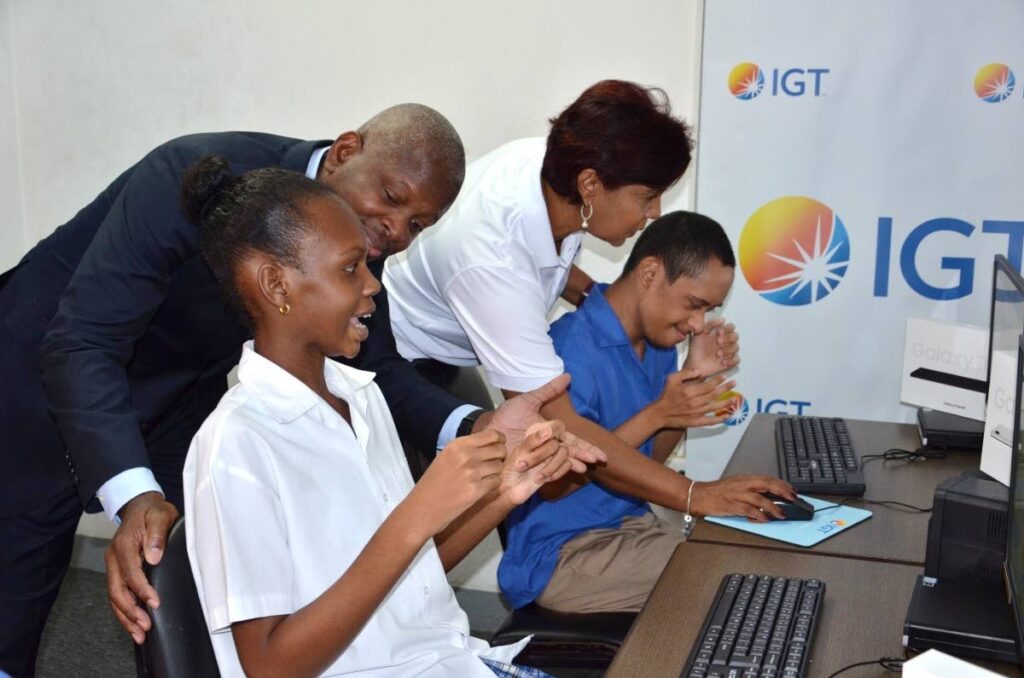 Dexter W Thomas, IGT general manager TT; and Shavindra Tewarie-Singh, IGT people and transformation regional senior manager for the Caribbean, assist these eager-to-learn students using the desktop computers donated to the Immortelle Centre through IGT’s After School Advantage programme. - 