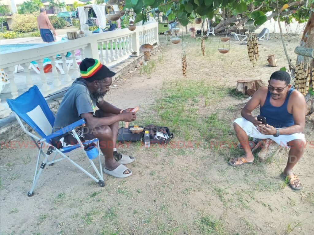 Craft vendor Blacks, left, sits at Turtle Beach, Tobago with a friend on Friday, after witnessing a shark attack on Peter Smith, 64, of England earlier that day. PHOTO BY COREY CONNELLY - 