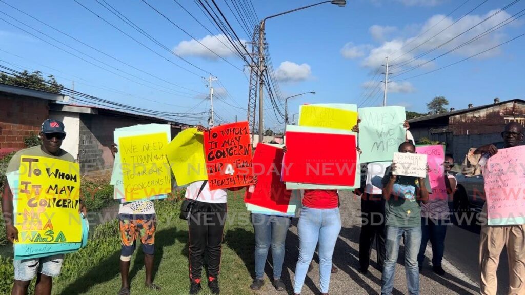 HEAR US: Residents from Beetham Gardens hold up placards during an early-morning protest on May 2 over leaking sewer lines which cause raw faeces to flow onto the roads and into houses. - Photo by Enrique Rupert