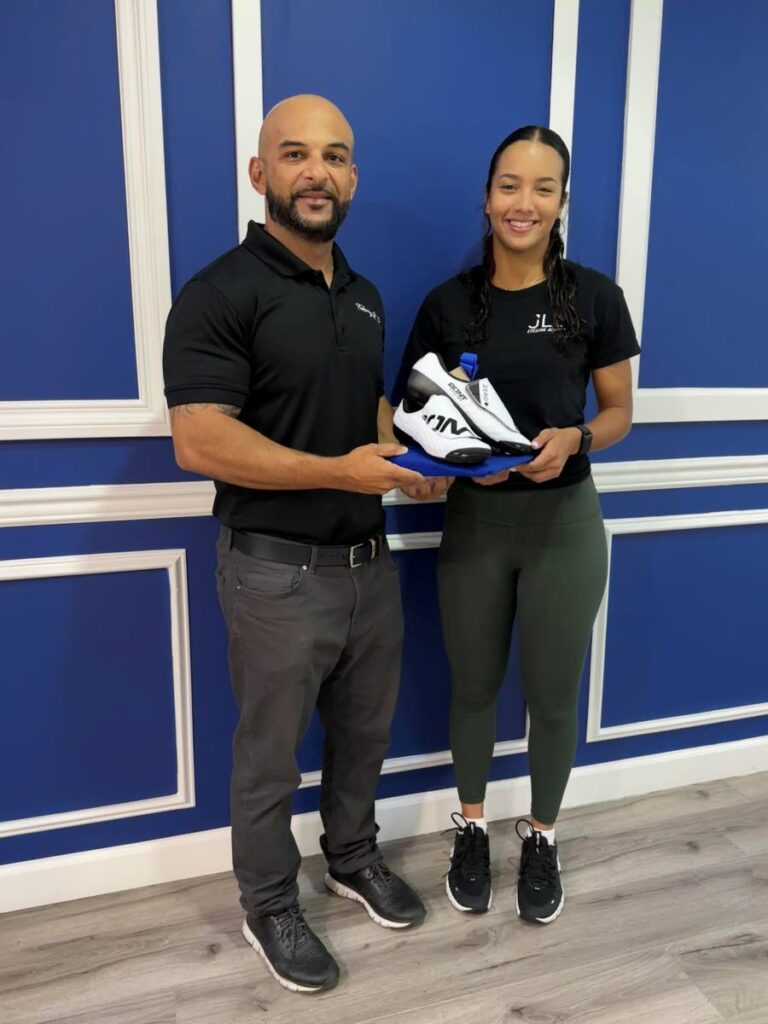 Dean Fakoory, director of The Fakoory Group of Companies, hands over a special racing shoe to national cyclist Makaira Wallace. - 