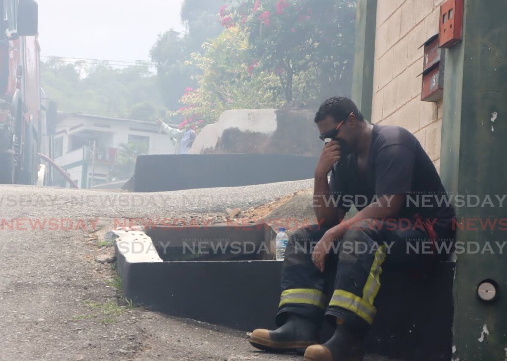 OVERWHELMING: A fire officer uses a face mask while trying to catch his breath at the scene of a house fire at Moses Avenue, San Juan on May 9.  - Photo by Ayanna Kinsale