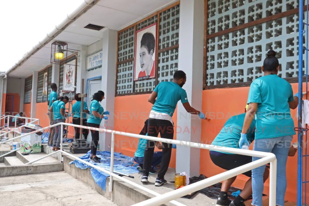 Republic Bank employees paint the front entrance of the St John’s Girls’ RC School in Diego Martin on May 20. - Photo by Venessa Mohammed