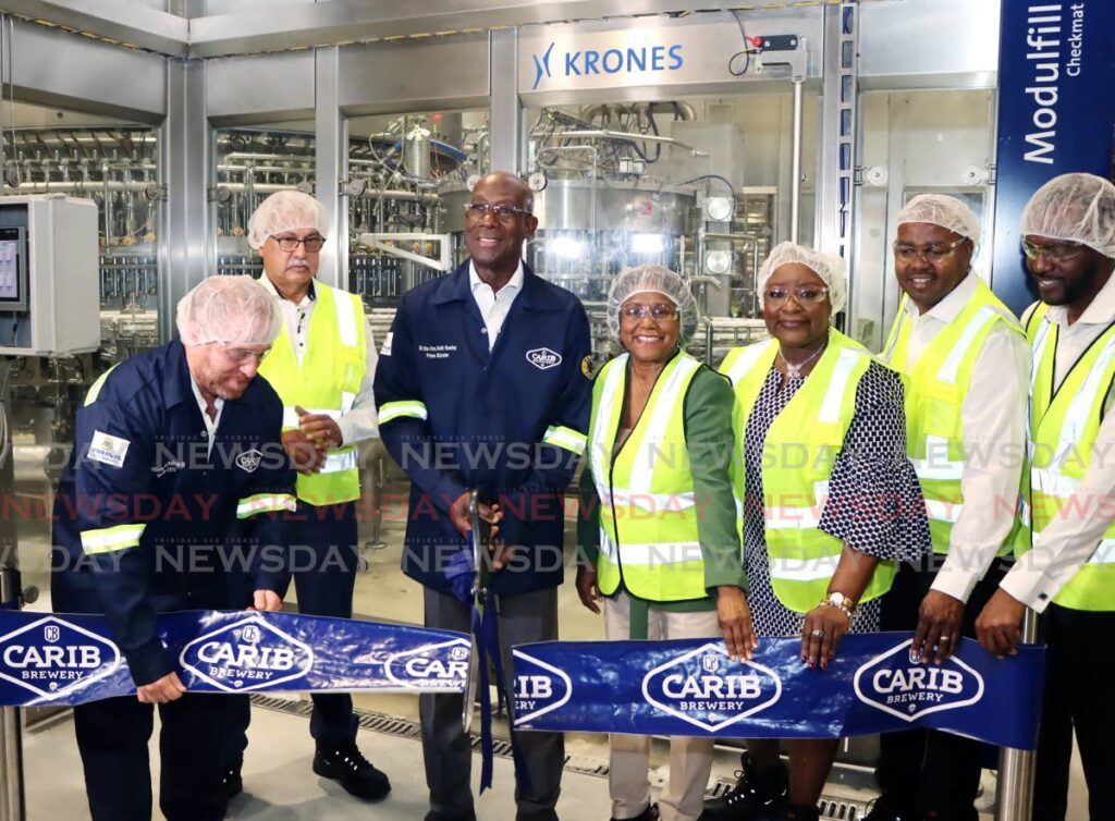 Prime Minister Dr Keith Rowley, centre,  cuts the ribbon at Carib's new manufacturing line 7 at Carib Brewery, Champs Fleurs on May 21.  Also in the photo are, from left,  group CEO ANSA McAL Ltd Anthony Sabga III, Minister of Health Terrence Deyalsingh, Minister of Trade and Industry Paula Gopee-Scoon, Minister of Housing and Urban Development Camille Robinson-Regis, Minister of Youth Development and National Service Foster Cummings, and Minister of Public Utilities Marvin Gonzales. - Photo by Ayanna Kinsale