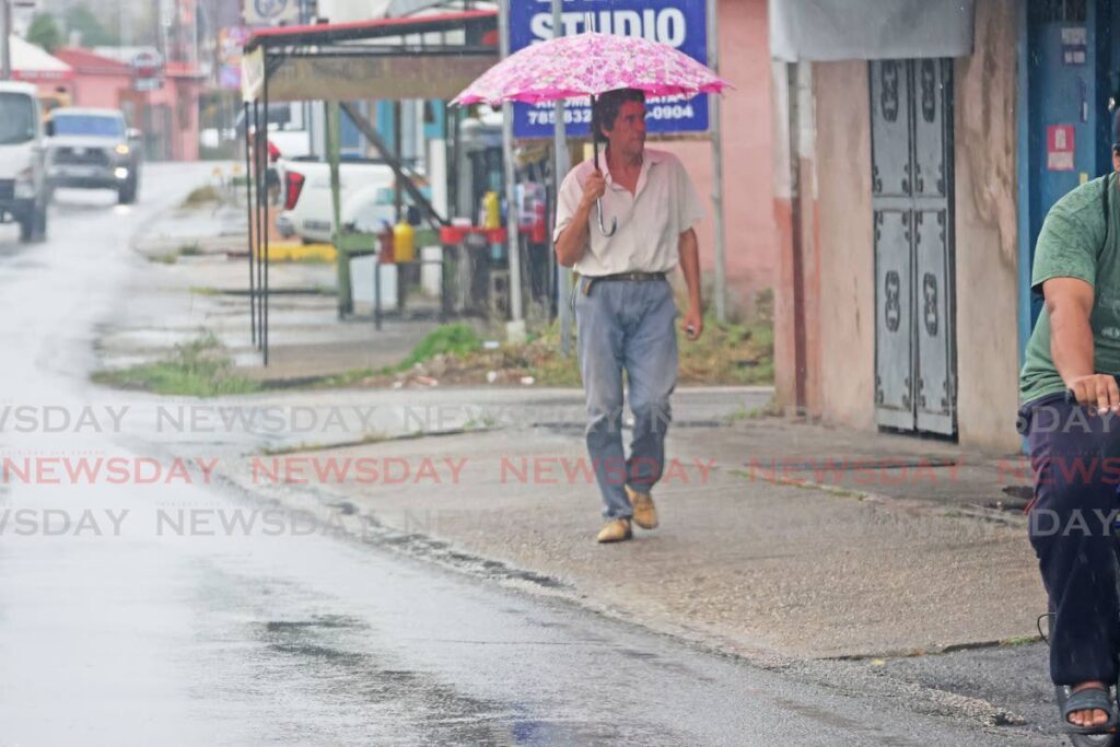 A man takes shelter as he walks along the Southern Main Road, Couva during a sudden downpour on May 25.  - Photo by Lincoln Holder 