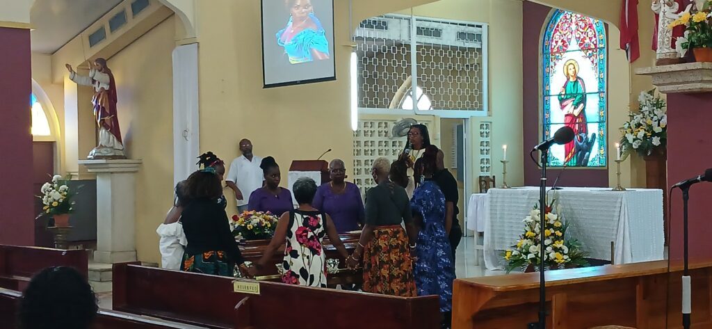 Minister Florence Warrick Joseph praying for the family of Nydia Byron as they surround her casket, at St John's Evangelist RC church, in Diego Martin. Photo by Joey Bartlett
