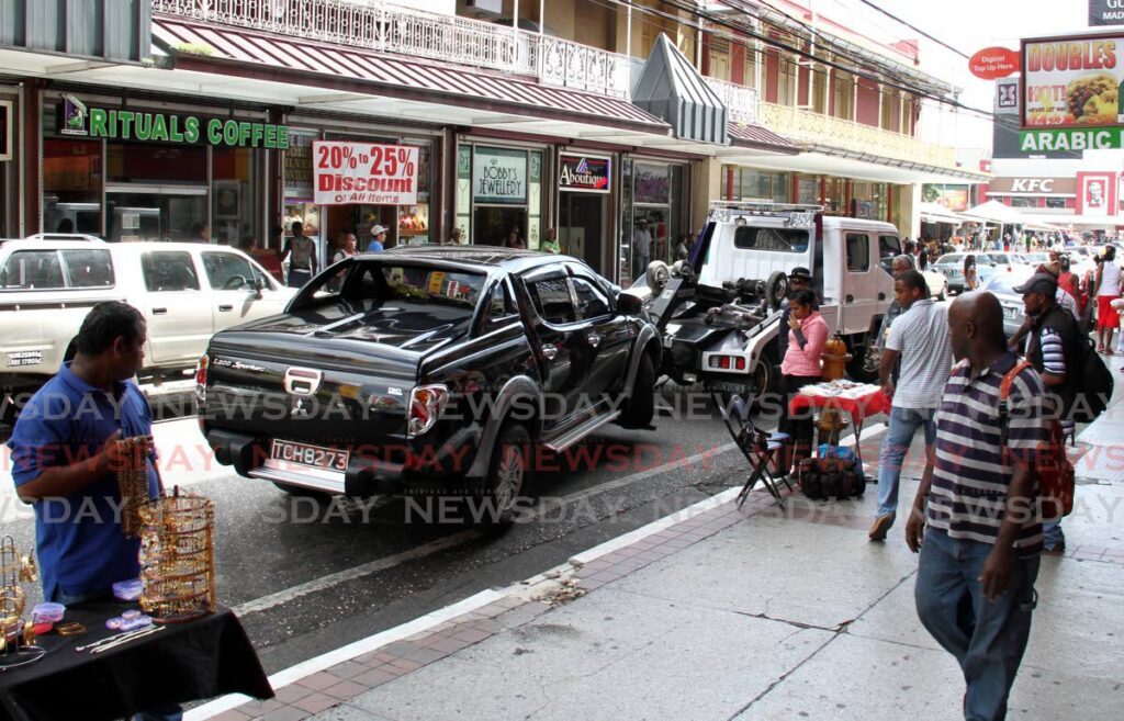 Onlookers watch as a vehicle is towed away on Frederick Street, Port of Spain. - File photo