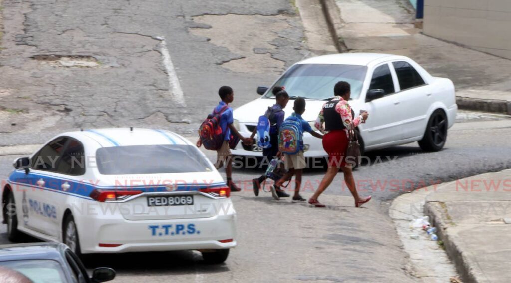 A policewoman, wearing a bulletproof vest, escorts school children after the Escallier St Jerome Anglican School in Gonzales, Belmont was dismissed early on June 3 following a mass shooting incident hours earlier on the evening of June 2. - Photo by Roger Jacob