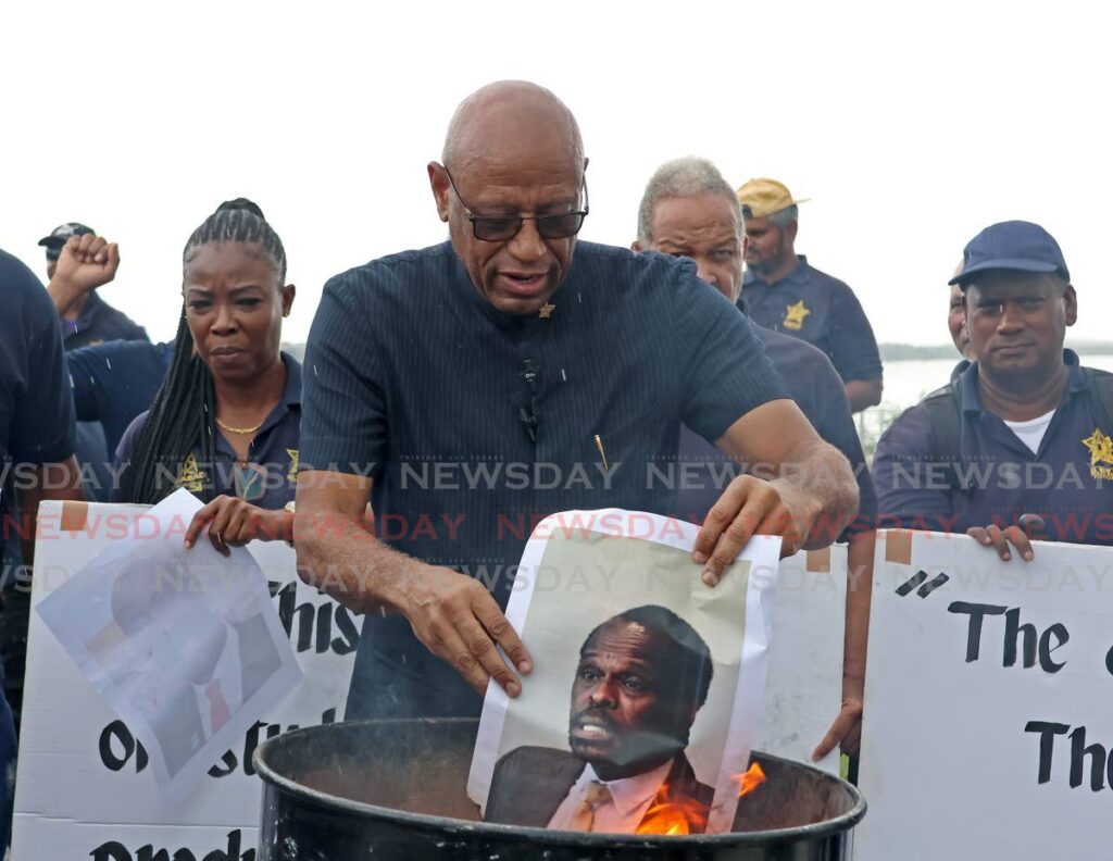 President general of the Oilfields Workers Trade Union (OWTU) Ancel Roget, centre, holds a burning picture of Minister of National Security Fitzgerald Hinds at a press conference at  Mosquito Creek in La Romaine on July 25. - Photo by Venessa Mohammed