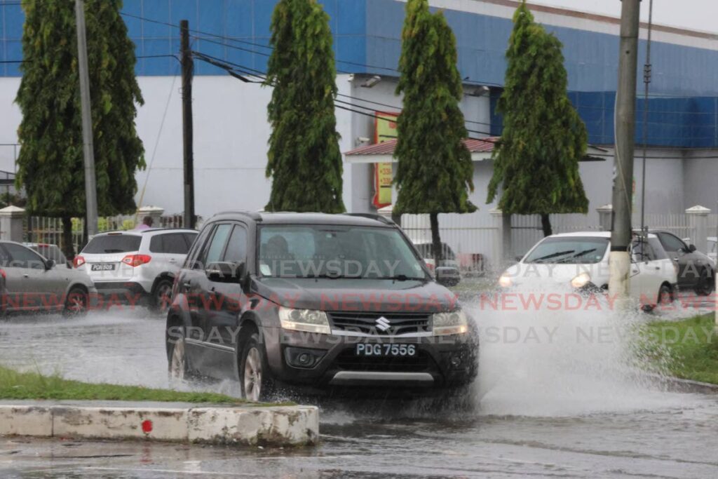 Motorists drive through flood waters in the merging lane at the Piarco intersection along the Churchill Roosevelt Highway on July 25. - Photo by Roger Jacob