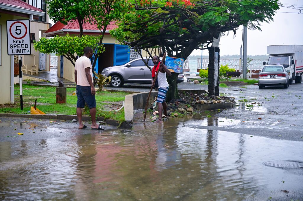 Men try to unclog a drain in Buccoo after flash flooding occurred during the passage of Hurricane Beryl on July 1. - Photo by Visual Styles